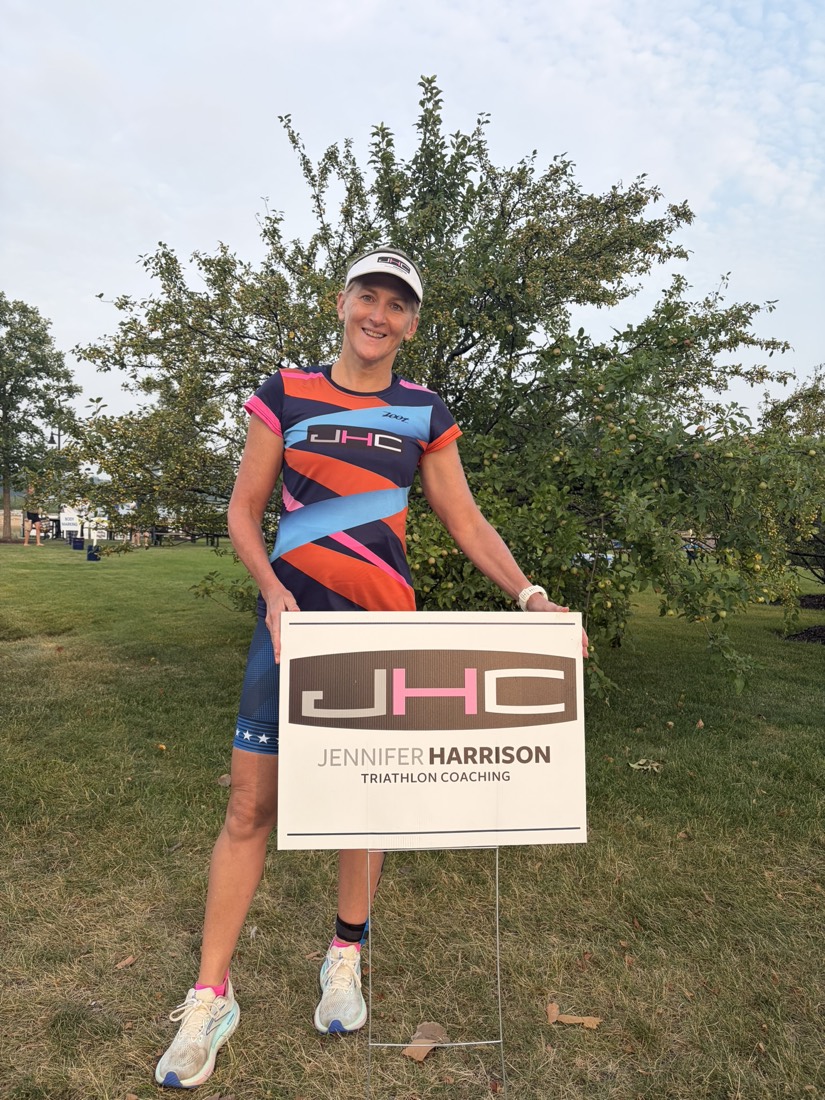 Jennifer Harrison in JHC race kit holding a Jennifer Harrison Triathlon Coaching sign