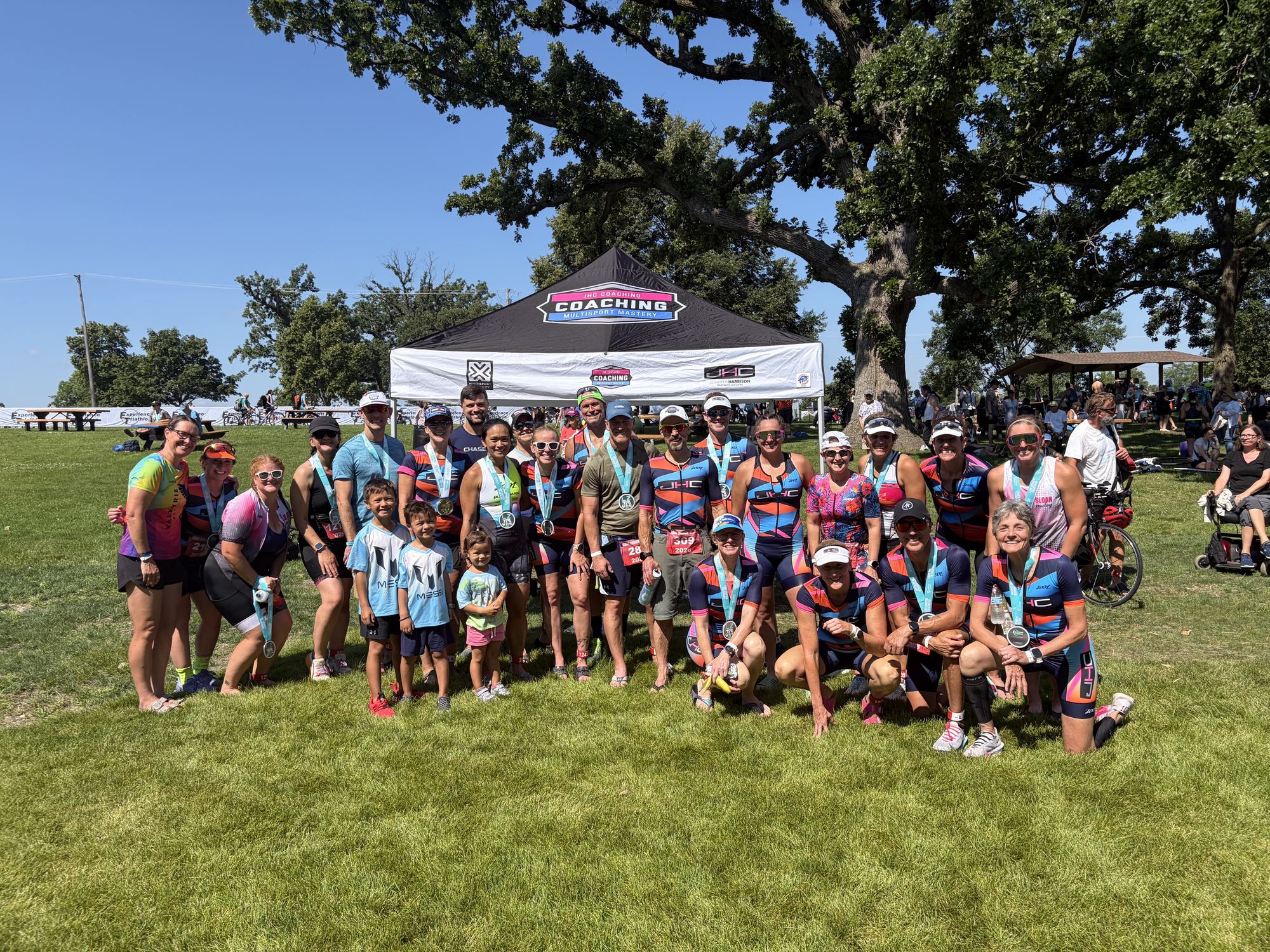 Team JHC athletes with their finisher medals gathered under the JHC Coaching tent after a race